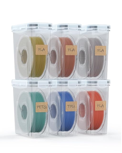 Six boîtes transparentes empilées sur deux rangées, chacune contenant une bobine avec une étiquette kraft marquée PLA, PETG ou TPU