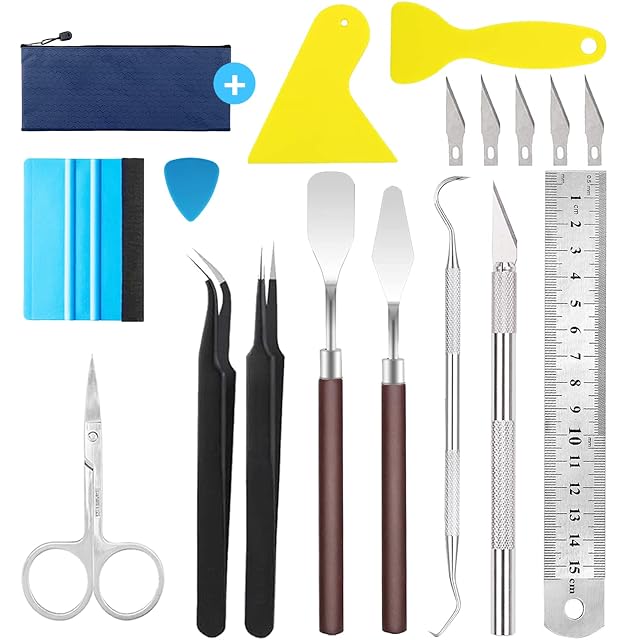 Outils disposés : pochette zippée, deux grattoirs jaunes, une raclette à bord feutré, une pointe, cinq lames, une pince, deux spatules, un crochet, un cutter, une règle en acier et des ciseaux